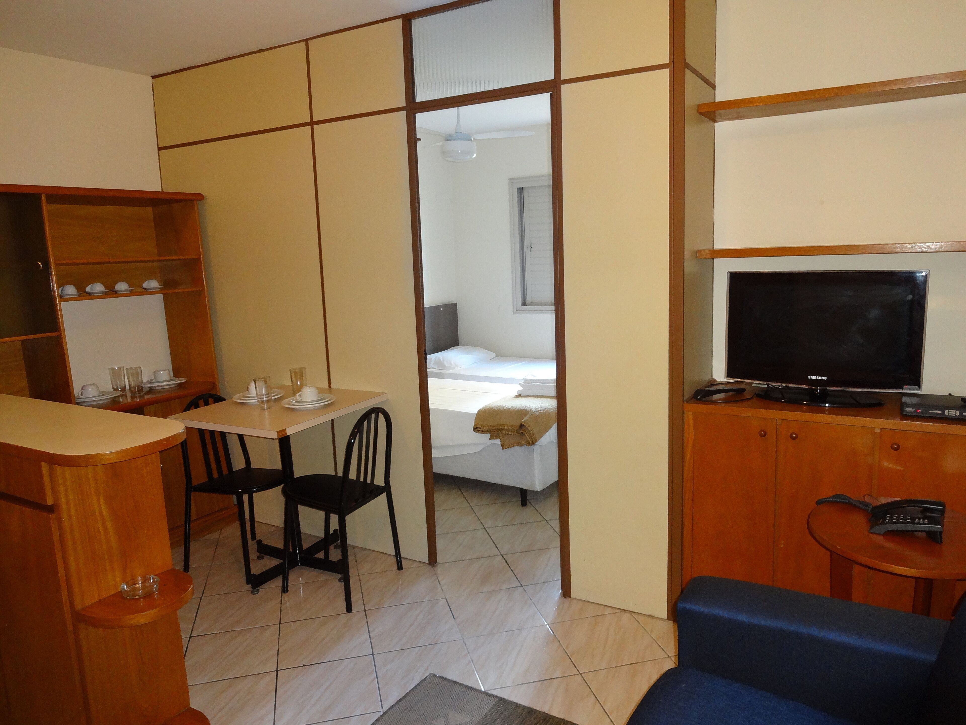Una habitación de hotel compacta con zona de comedor, cama, televisor y un pequeño rincón de descanso.