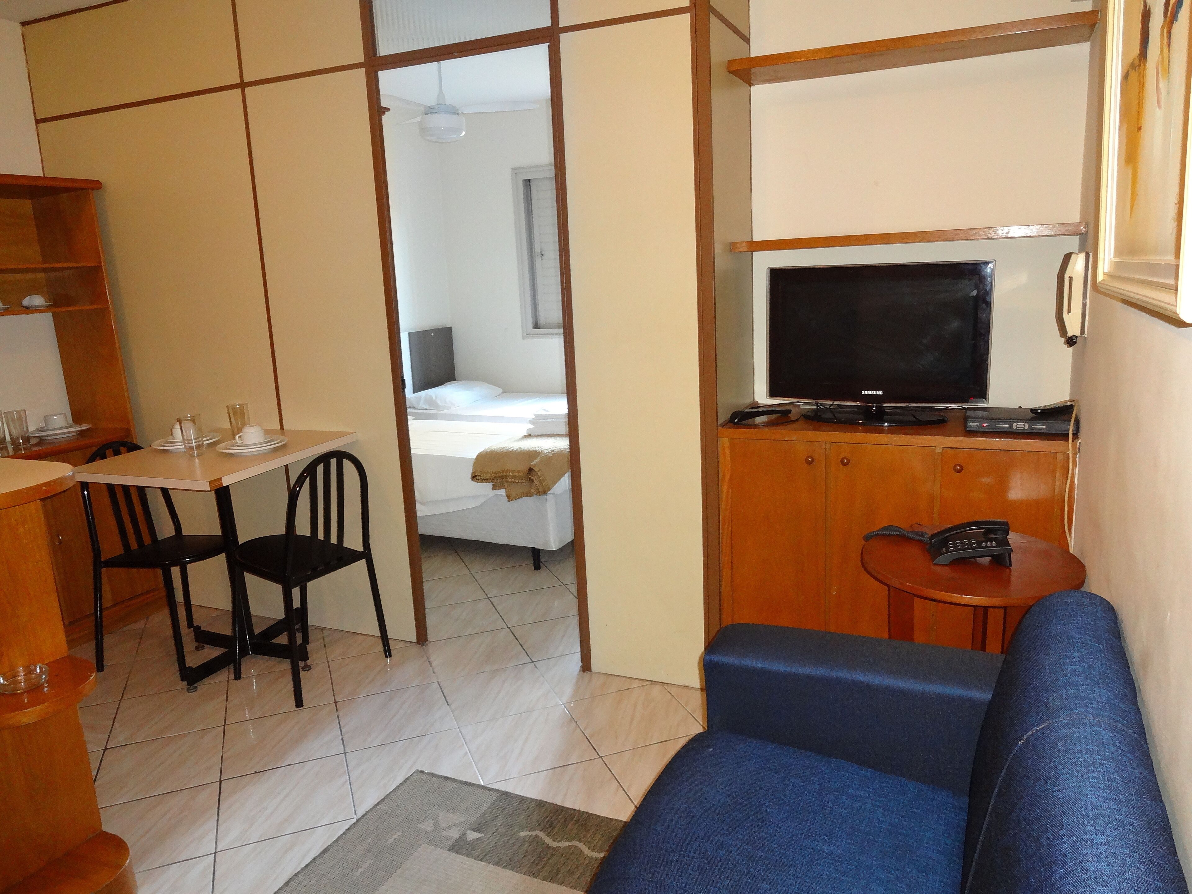 A compact room with a bed, a TV, a small table with chairs, and a sofa.