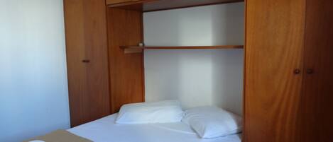 Quarto pequeno com uma cama de solteiro, armários de madeira e carpete bege.
