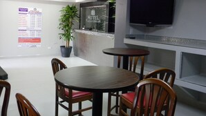 Un hall de hotel con una recepción, una planta en maceta, un televisor de pantalla plana y varias mesas y sillas de madera.