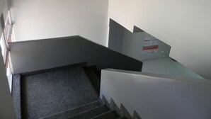 Una escalera con un rellano alfombrado y una pared blanca con un ventanal pequeño.