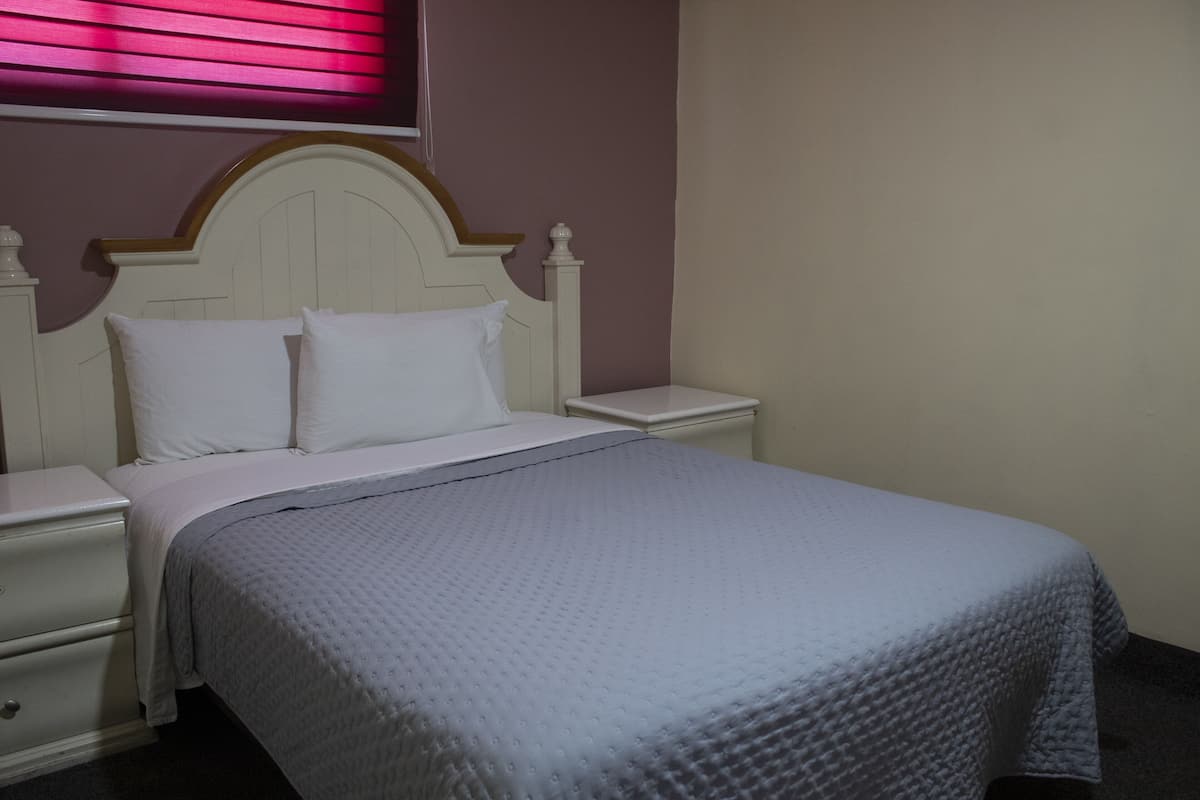 Una cama bien hecha con cabecera blanca y almohadas a juego, una mesita de noche blanca y una mesita auxiliar.