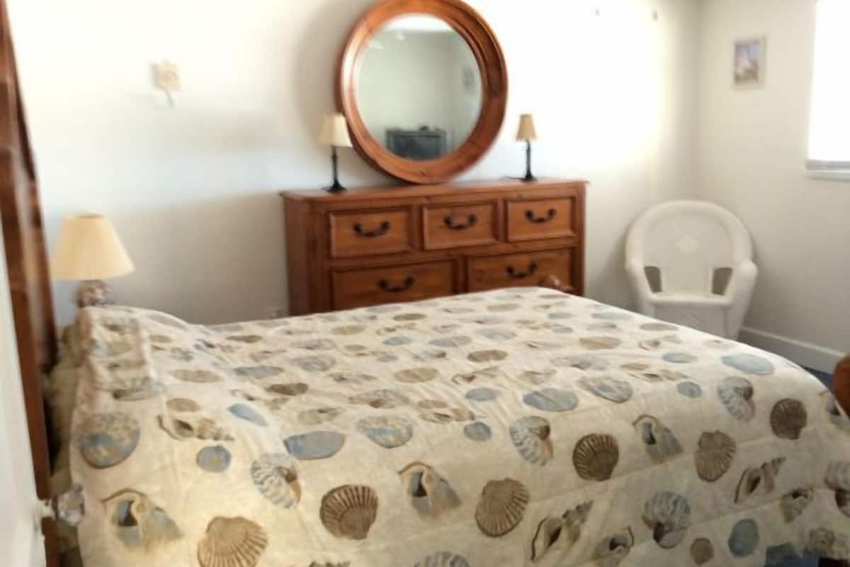 Une chambre à coucher comprenant un lit, une commode avec des tiroirs, un miroir, une chaise et une lampe.