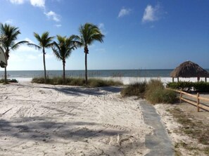 A sandy beach with palm trees and a thatched-roof structure.