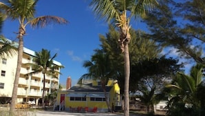 A beachfront property with a yellow building, palm trees, and a sandy beach. - Red Coconut RV Park (Fort Myers Beach)