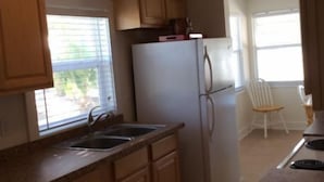 A kitchen with wooden cabinets, a white refrigerator, a ceiling fan, and a window with blinds. - Red Coconut RV Park (Fort Myers Beach)