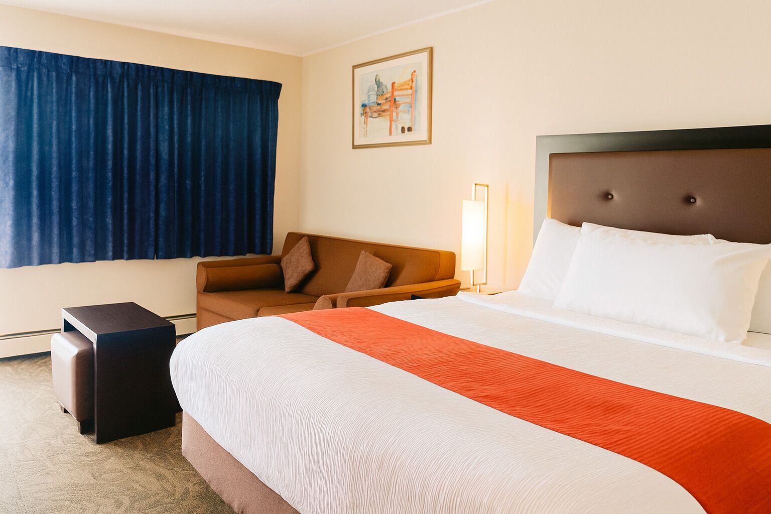 Habitación de hotel con una cama grande, un sofá, una mesita y un cuadro en la pared.