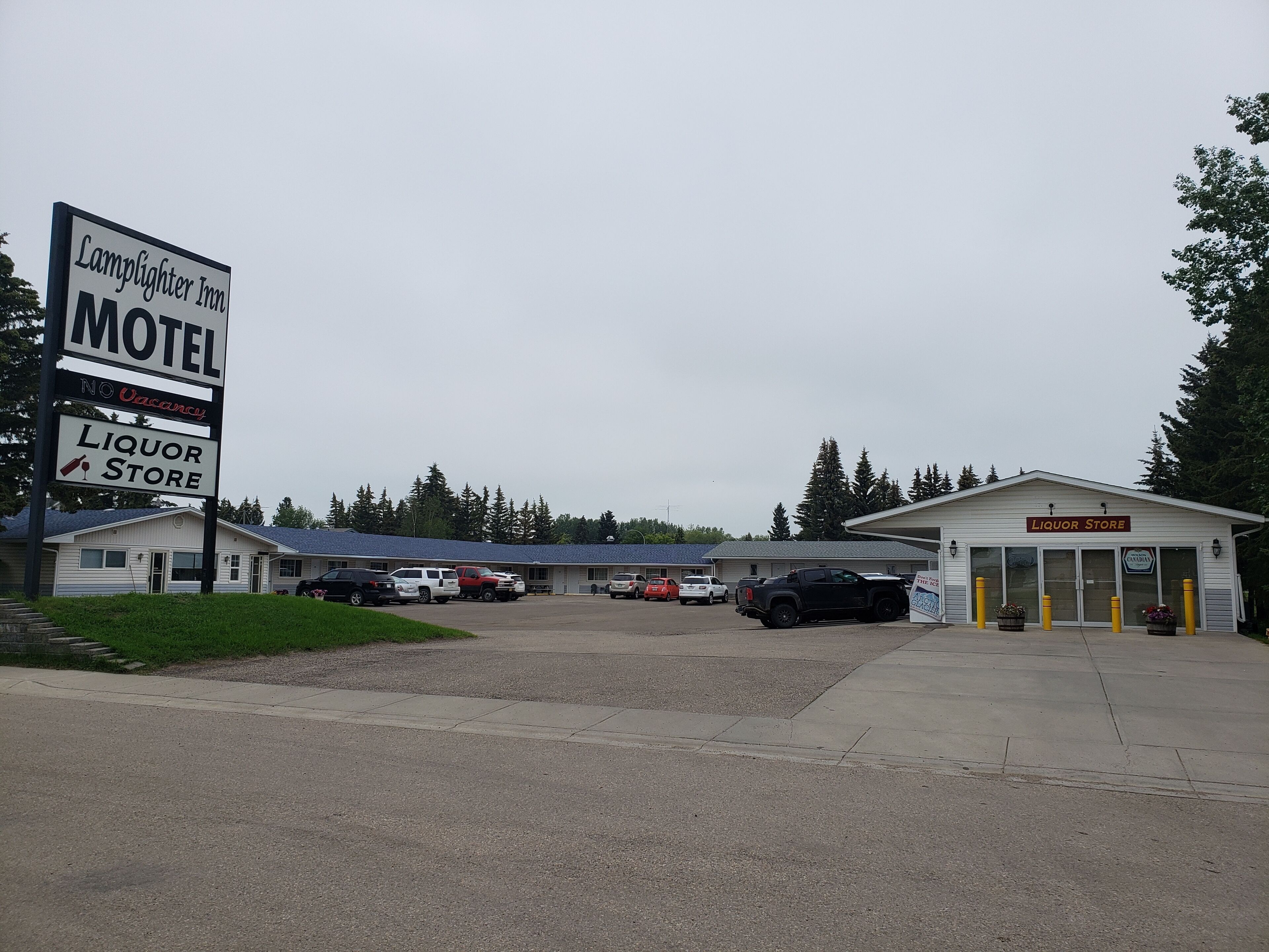 A motel with a liquor store, multiple parked vehicles, and a building with a signboard.