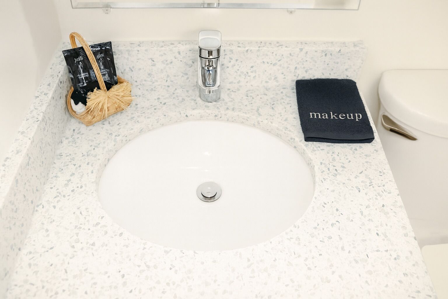Un baño con un lavamanos blanco, una toalla y un neceser sobre la encimera.