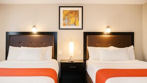 A hotel room with two beds, each with a headboard, a nightstand between them, and a framed picture on the wall.