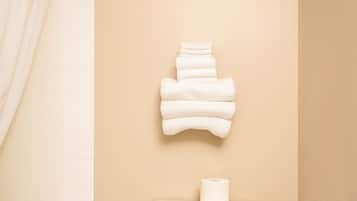 A bathroom with a toilet, a towel rack with folded towels, a shower curtain, and a toilet paper holder.