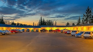 A hotel with a parking lot filled with cars, surrounded by trees and a sunset sky.