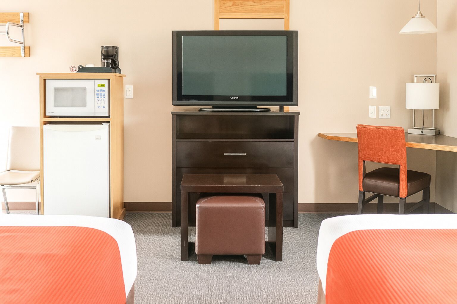 A hotel room with two beds, a desk with a chair, a television, a microwave, and a refrigerator.