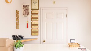 A reception area with a white desk, a beige sofa, a plant, framed awards, a 'Motel' sign, and a door.