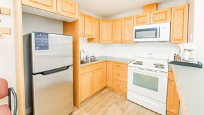 A compact kitchen with wooden cabinets, a stainless steel refrigerator, a microwave, a stove, and a coffee maker.