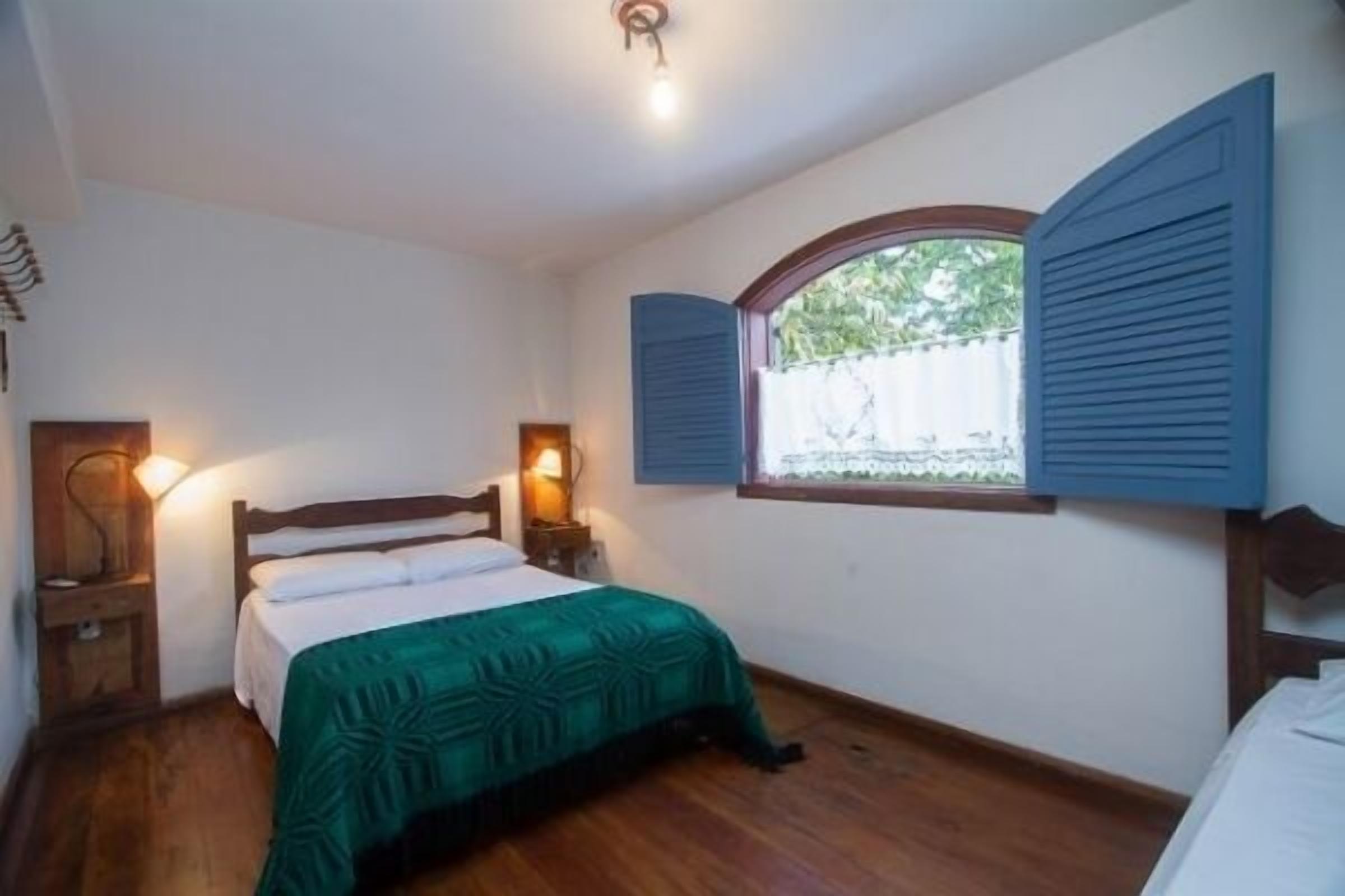 Una camera da letto con un letto in legno, una finestra con persiane, una lampada da comodino e vista sul verde.