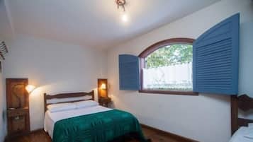 Una camera da letto con un letto in legno, una finestra con persiane, una lampada da comodino e vista sul verde.