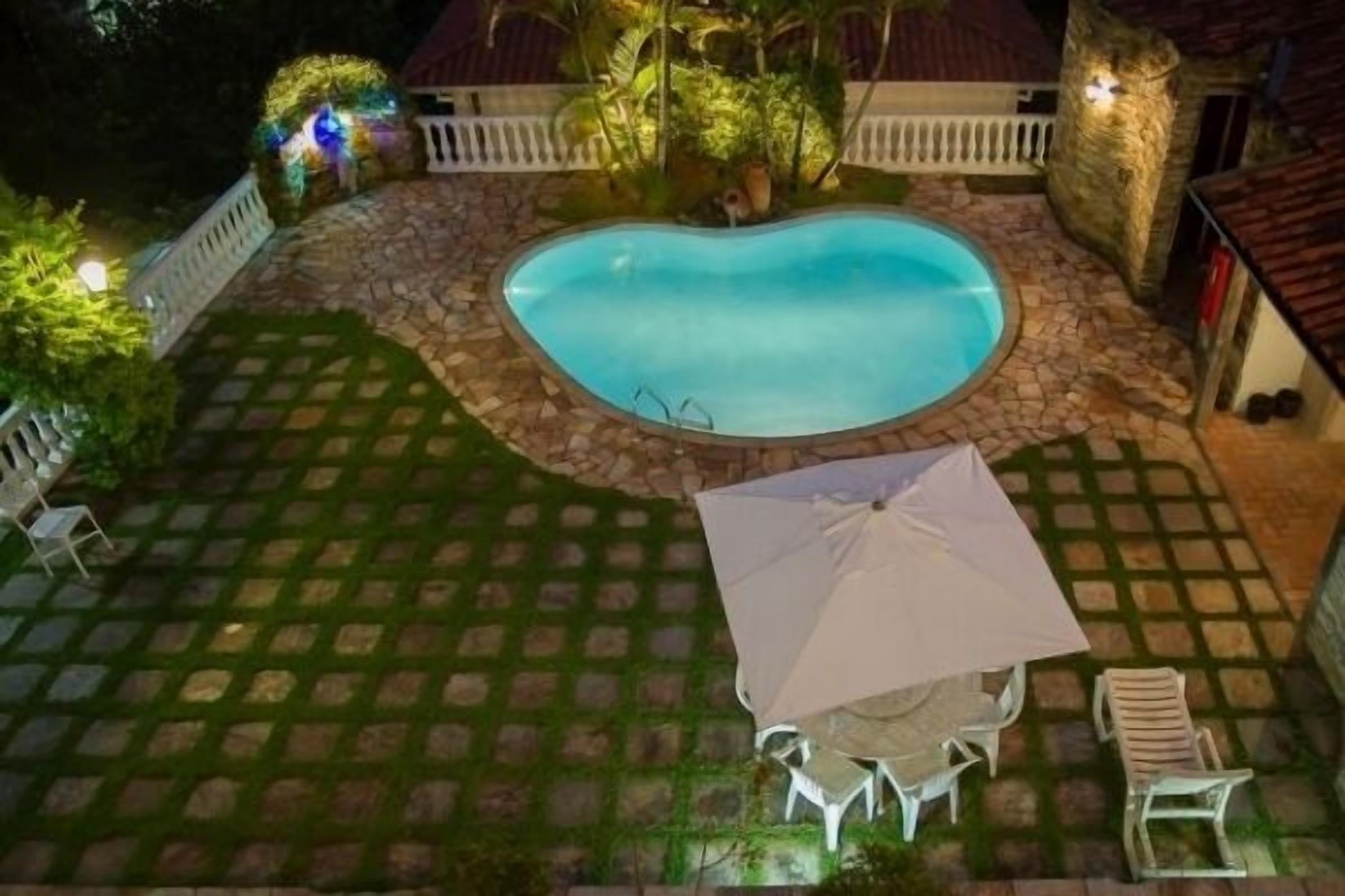 Una piscina rodeada de baldosas de piedra, una cerca blanca y un pequeño patio con una mesa y sillas.