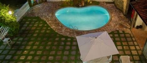 Una piscina rodeada de baldosas de piedra, una cerca blanca y un pequeño patio con una mesa y sillas.