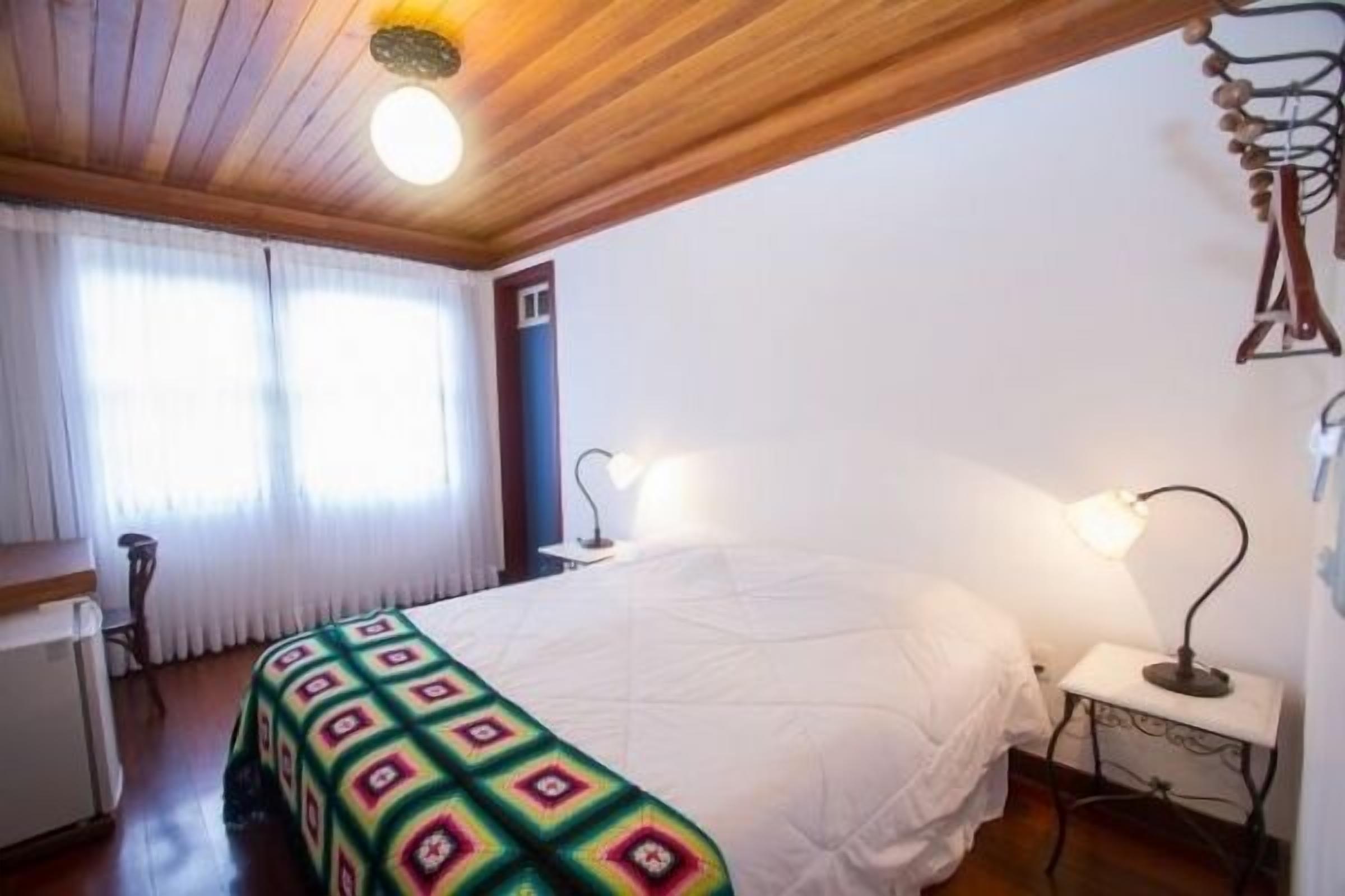 A bedroom with a bed, a nightstand, a lamp, and a window with curtains.