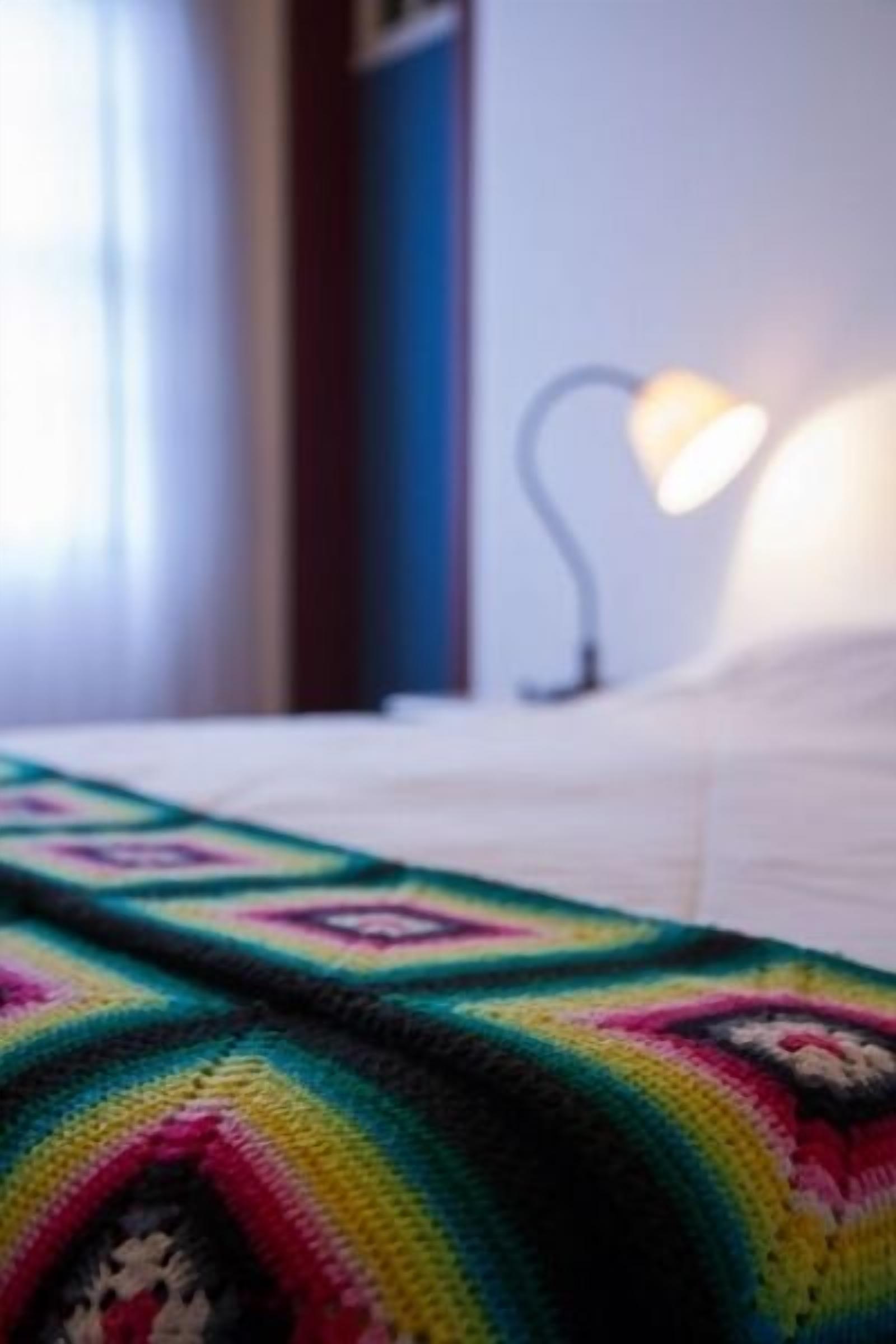 A bed with a colorful blanket and a bedside lamp.