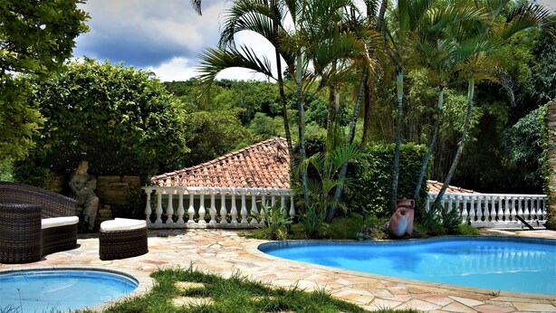 Une piscine dotée d’une terrasse carrelée, entourée d’une végétation luxuriante et d’un mur en pierre.