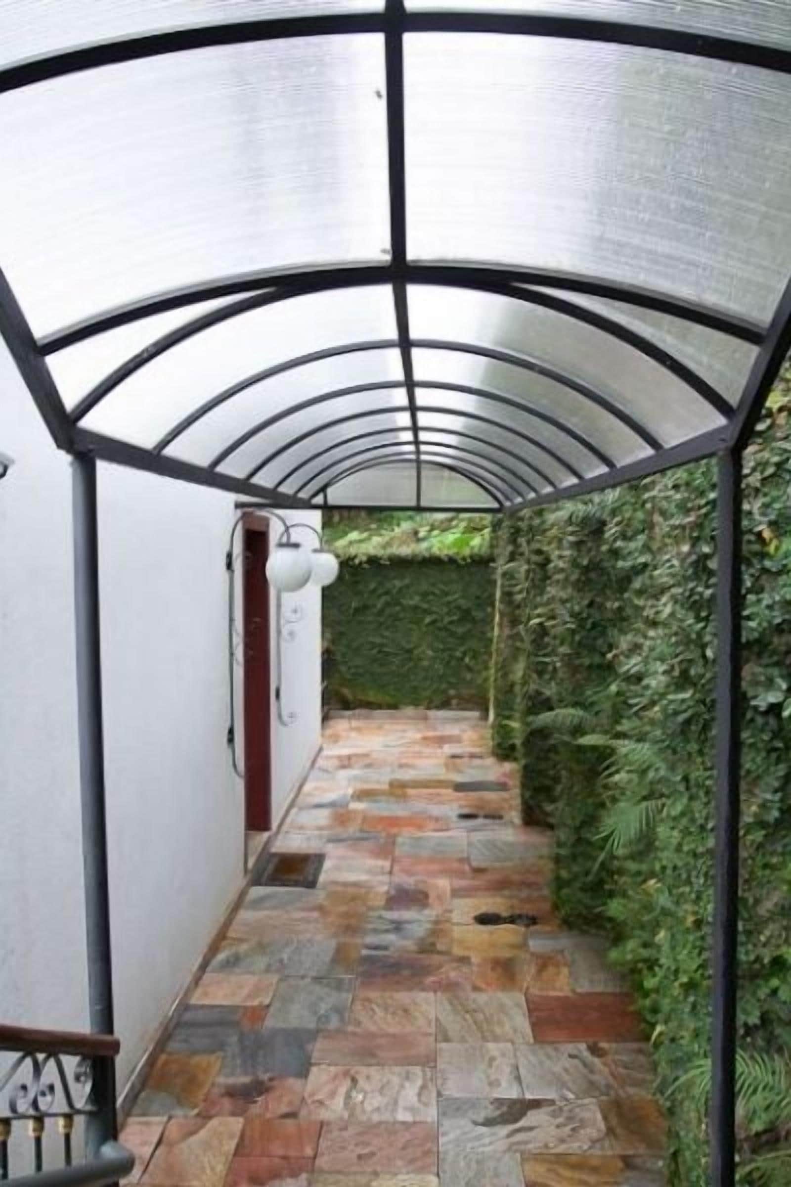 A covered walkway with stone flooring and green foliage on the walls.