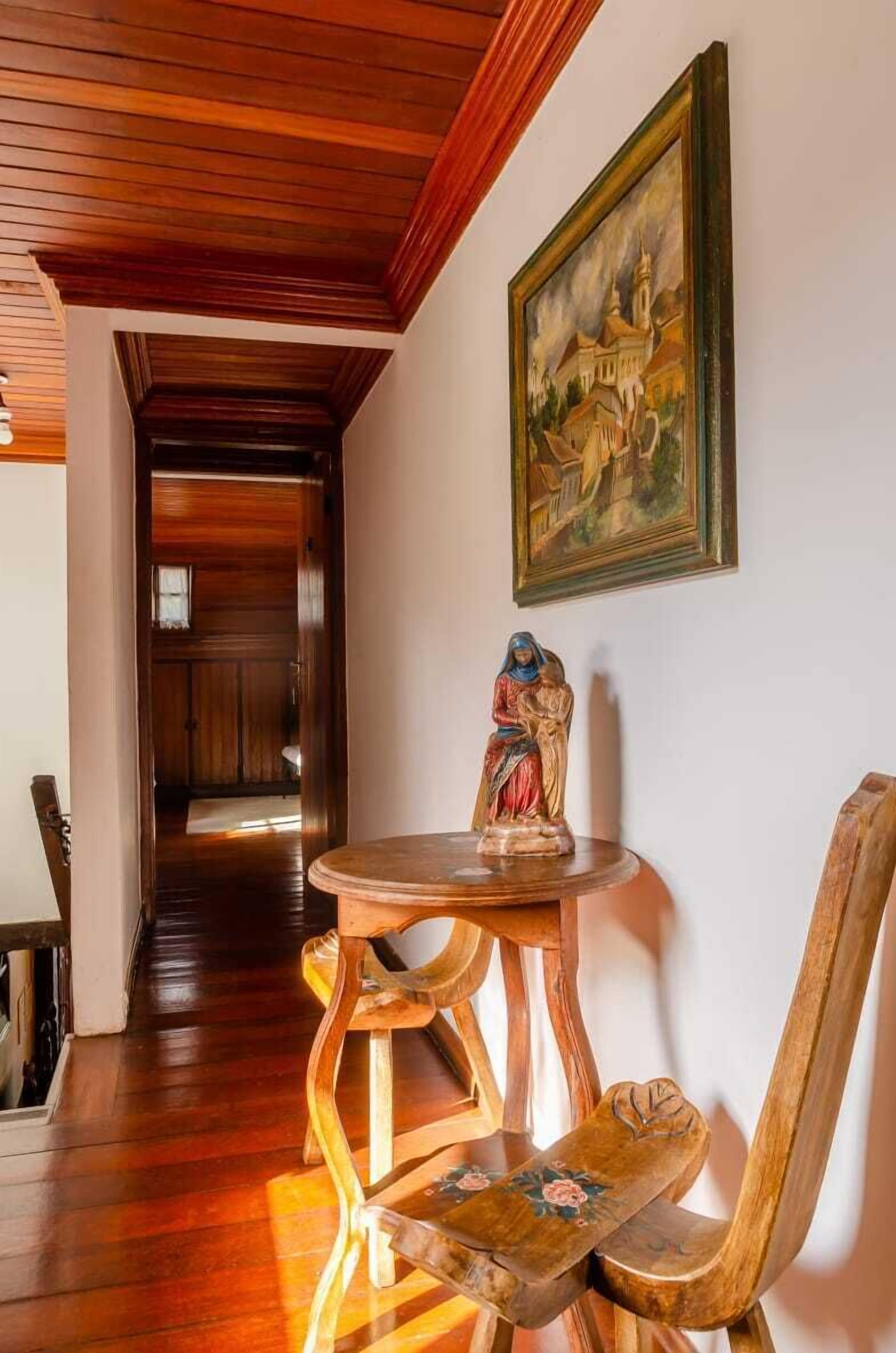 A wooden interior with a dining table and chairs, a statue, and a painting on the wall.