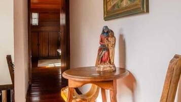 A wooden interior with a dining table and chairs, a statue, and a painting on the wall.