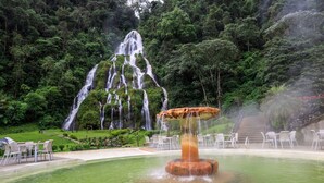 Uma fonte com água caindo em vários níveis, rodeada por um lago e área de estar ao ar livre.