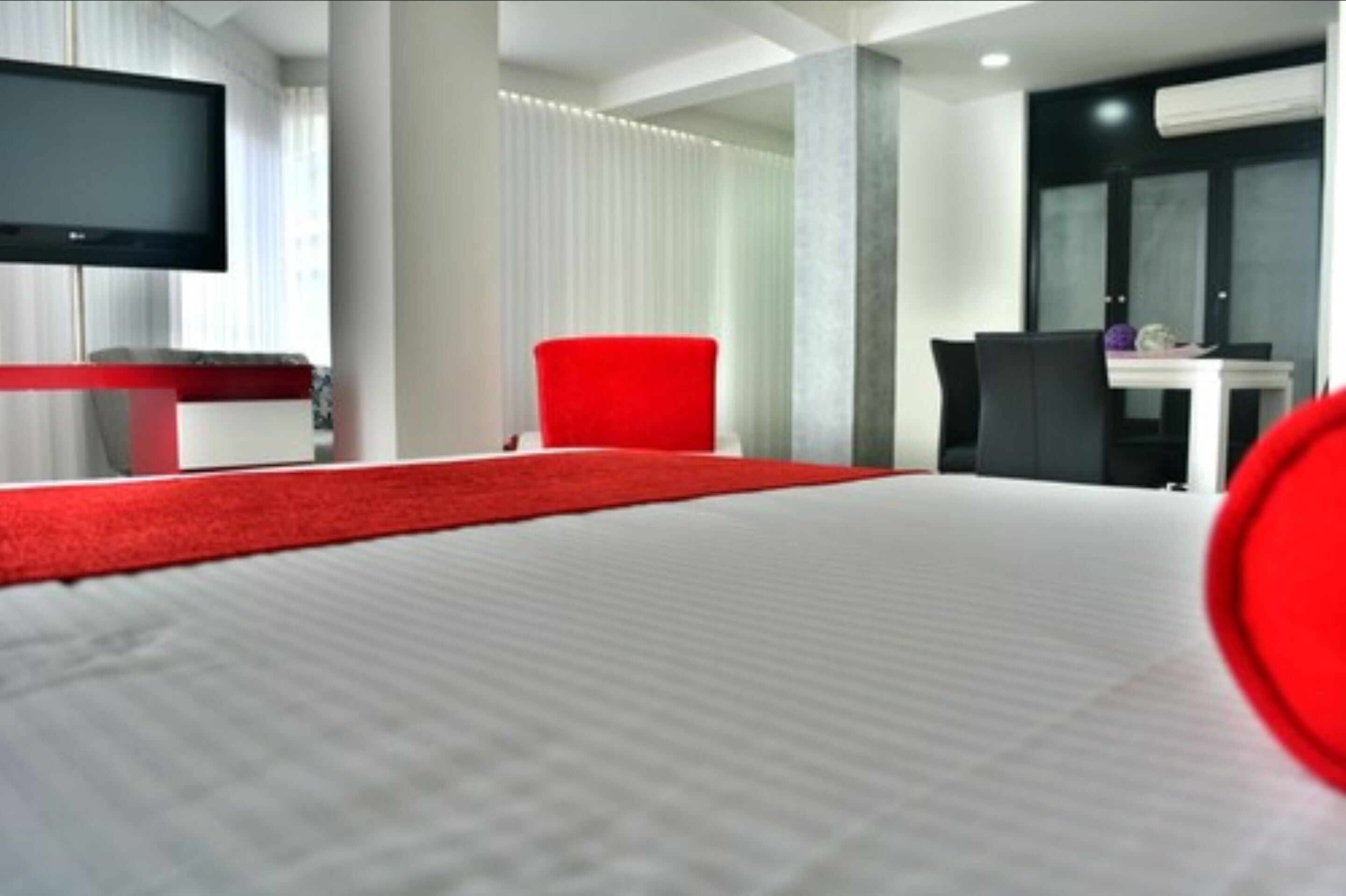 A modern hotel room with a large bed, a red chair, a desk, and a flat-screen TV.