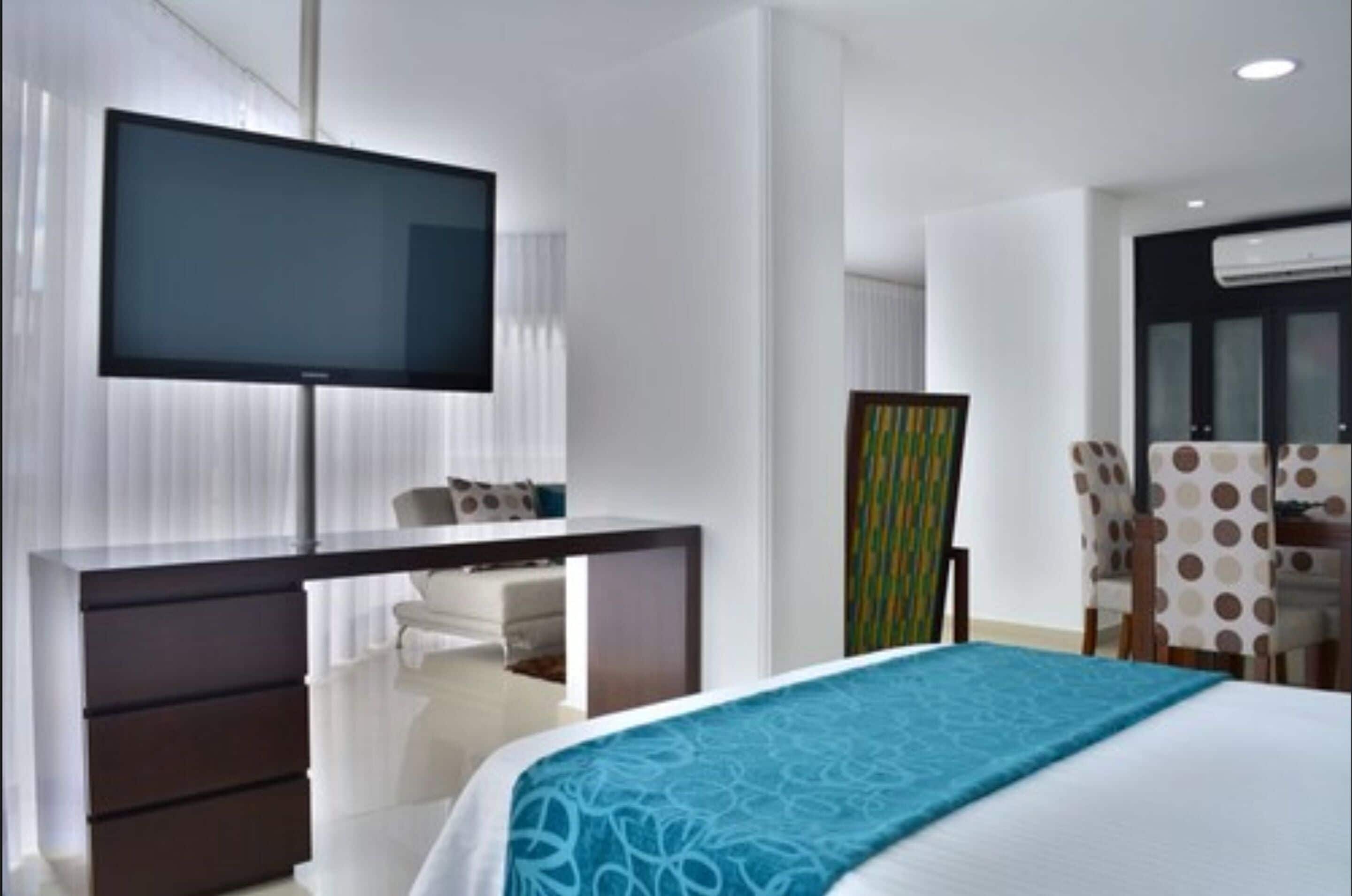 Una habitación de hotel moderna con una cama grande, un escritorio con televisor de pantalla plana, una silla y una mesa de comedor con mantel a lunares.