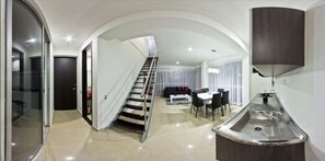 A modern interior with a staircase leading to a dining area, a kitchen with a sink, and a glass wall. - Hotel Monterosa Lofts (Pereira)