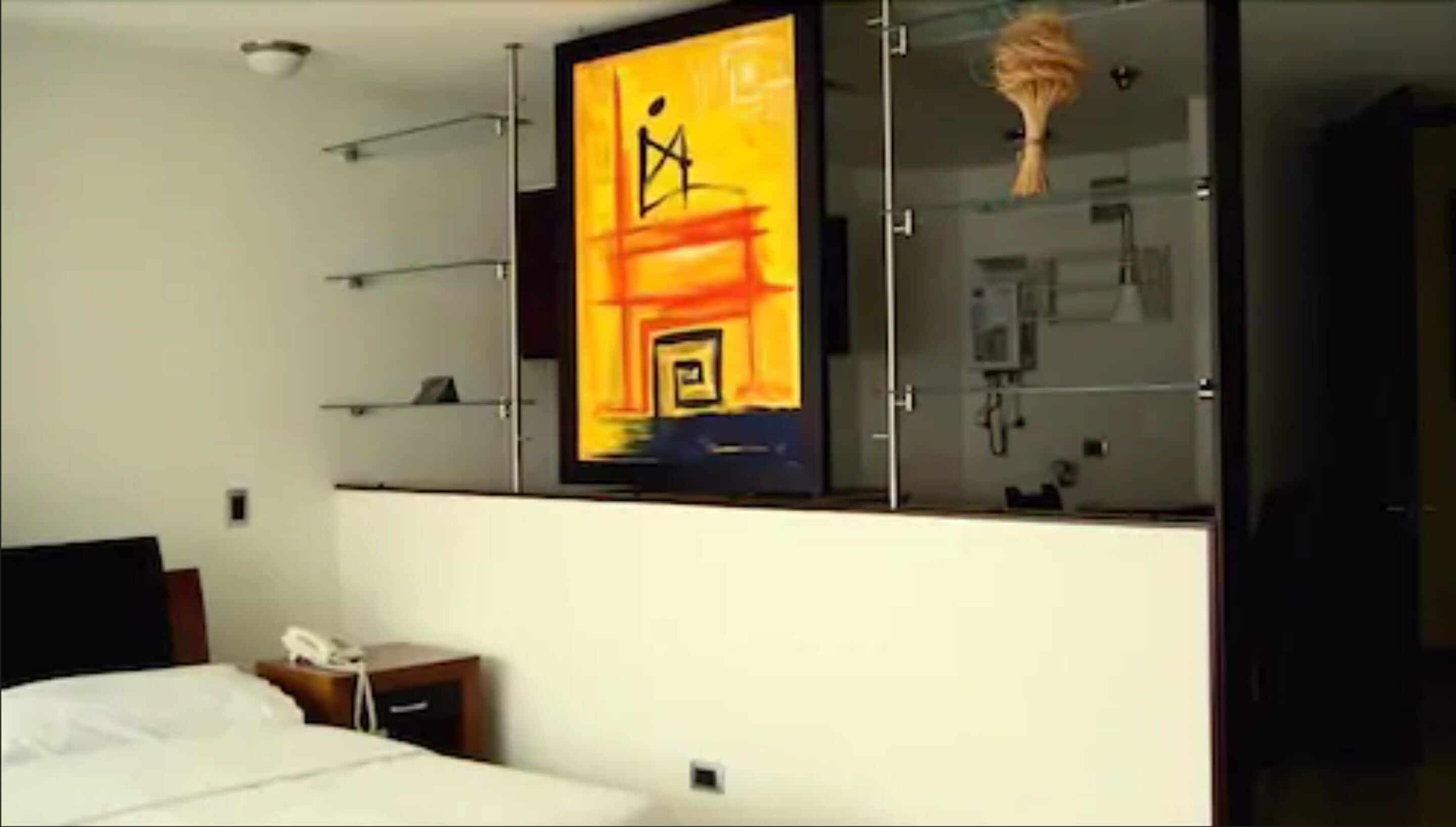 A hotel room with a bed, bedside table, and a wall-mounted TV displaying a colorful abstract image.