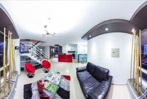 Una sala de estar moderna con un sofá de cuero negro, sillas rojas, una mesa de centro con revistas y una escalera que conduce a un nivel superior.