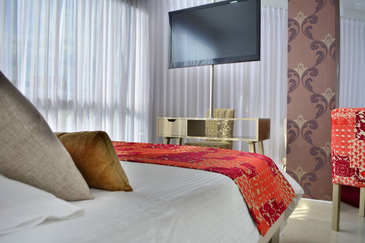 Ein Hotelzimmer mit einem Bett, einem an der Wand befestigten Fernseher, einem Schreibtisch und einem Stuhl.