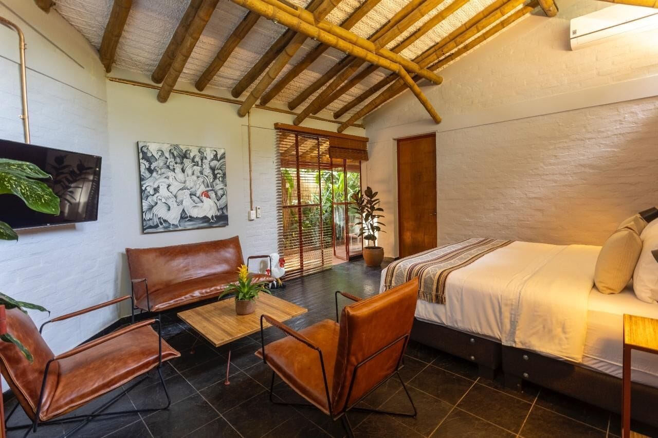 Une pièce comprenant un lit, un canapé, une table et des chaises. Il y a un tableau au mur et une fenêtre avec des stores.