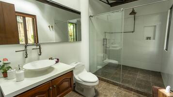 A modern bathroom with a large mirror, a sink, a toilet, and a glass-enclosed shower area.