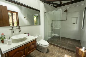 A modern bathroom with a large mirror, a sink, a toilet, and a glass-enclosed shower area.
