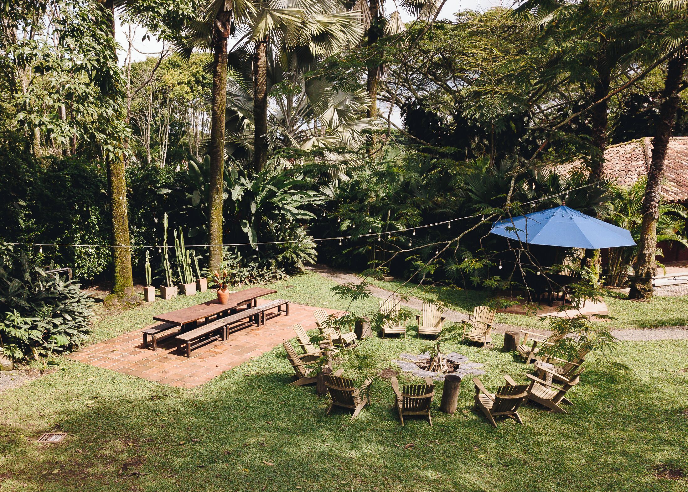 Un patio con muebles de madera, luces colgantes y un paraguas azul.
