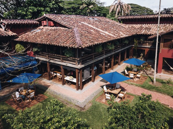 Un edificio tradicional de madera con techo de tejas, zona de estar al aire libre con mesas y sillas, y plantas en macetas.