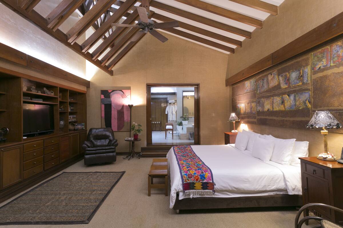 A spacious bedroom with a large bed, a television, a leather chair, and a ceiling fan.