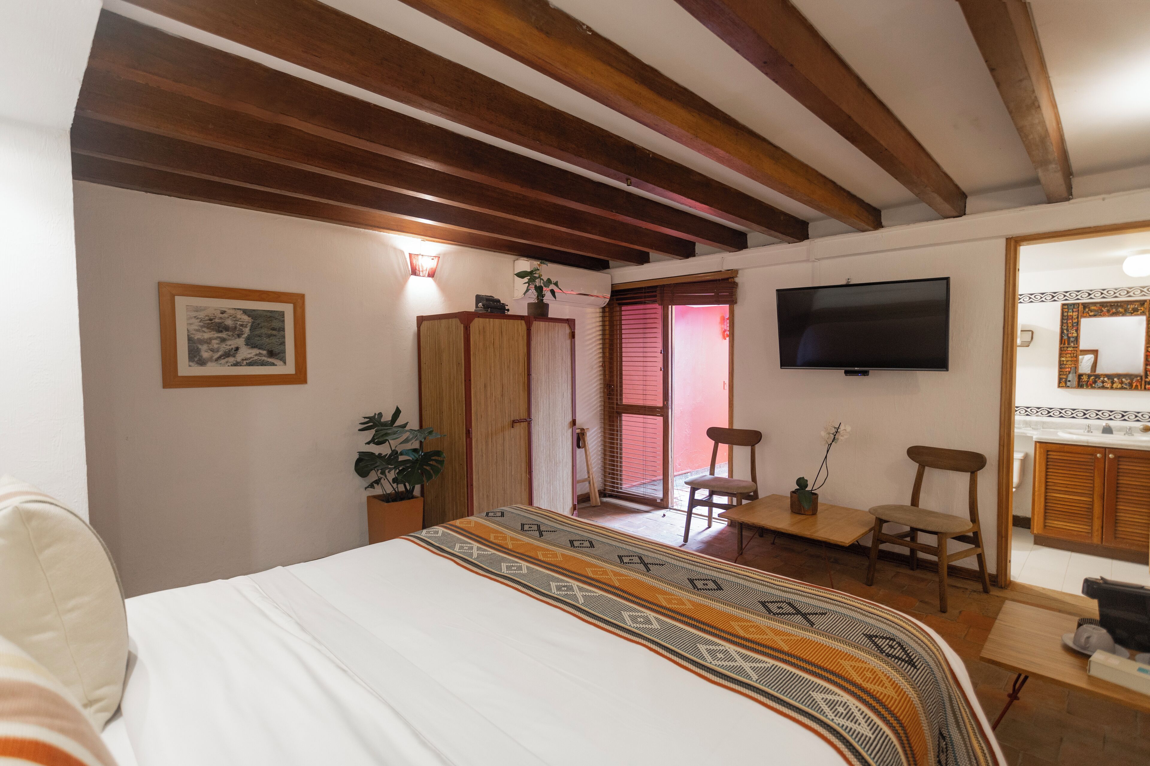Un dormitorio con cama, vigas de madera, televisor, escritorio y silla.