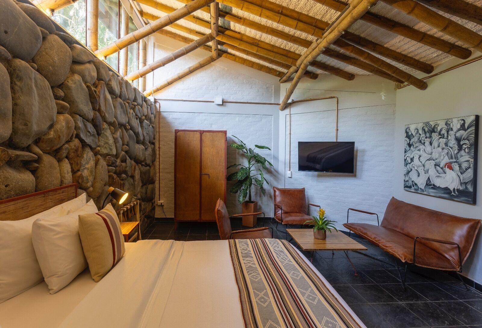 A bedroom with a stone wall, a bed, a TV, and a painting.