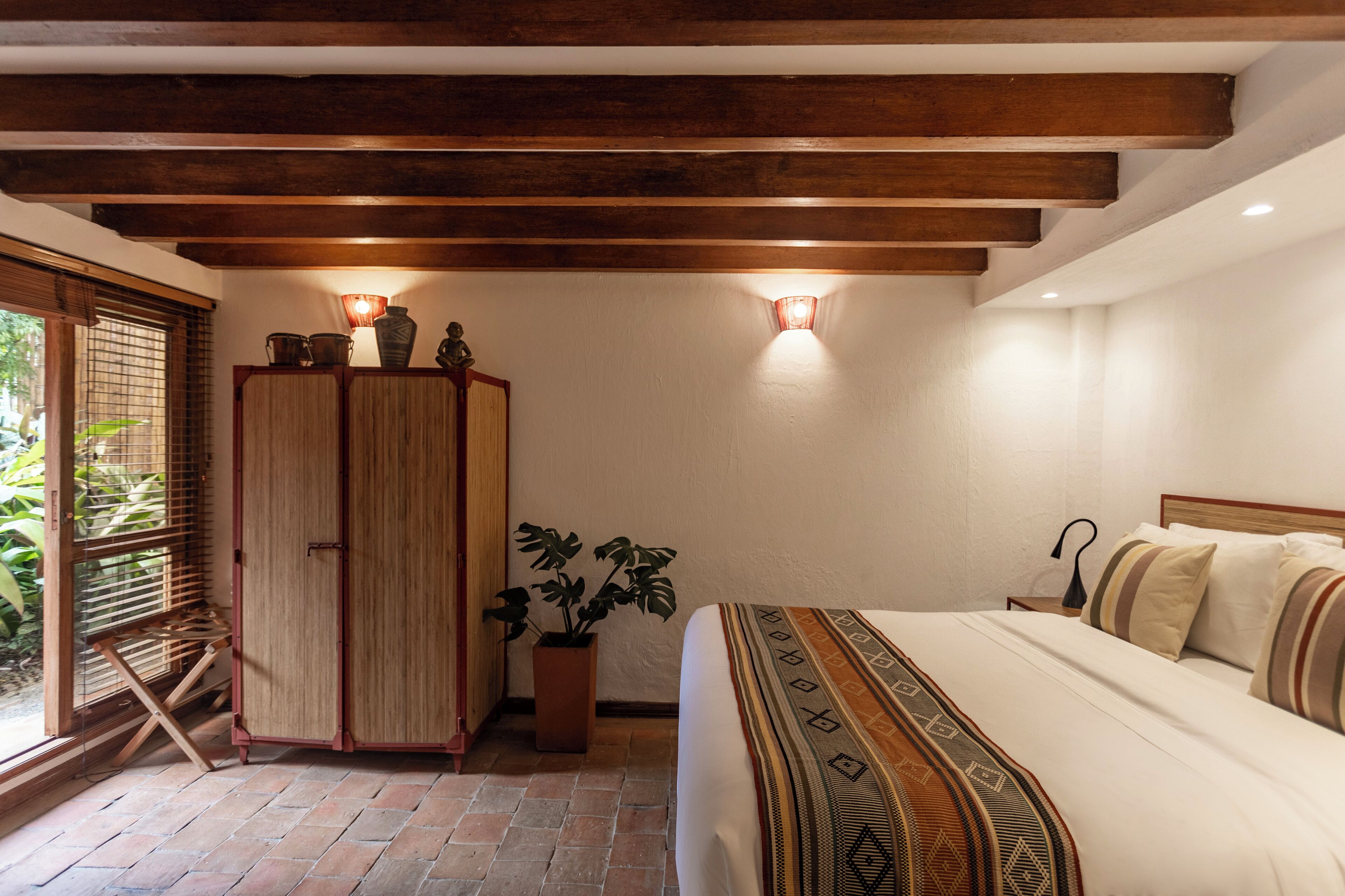 A bedroom with a bed, wooden wardrobe, potted plant, and two wall-mounted lights.