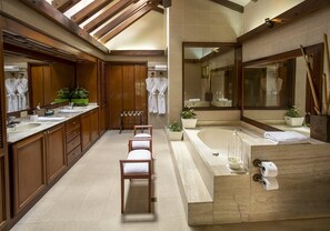 Un baño espacioso con una bañera grande, dos lavamanos, armarios de madera y un espejo.