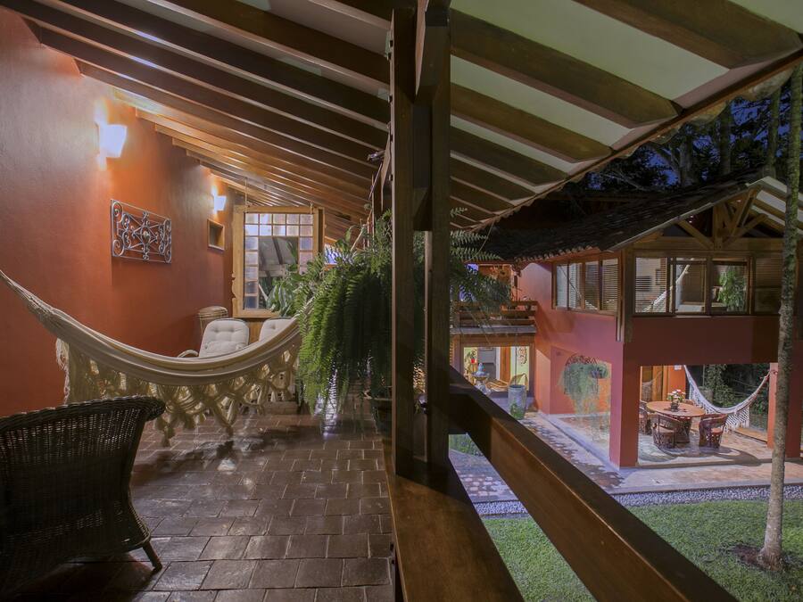 Un espacio al aire libre techado con una hamaca, muebles de mimbre y vista a un edificio de estructura de madera y techo de paja.
