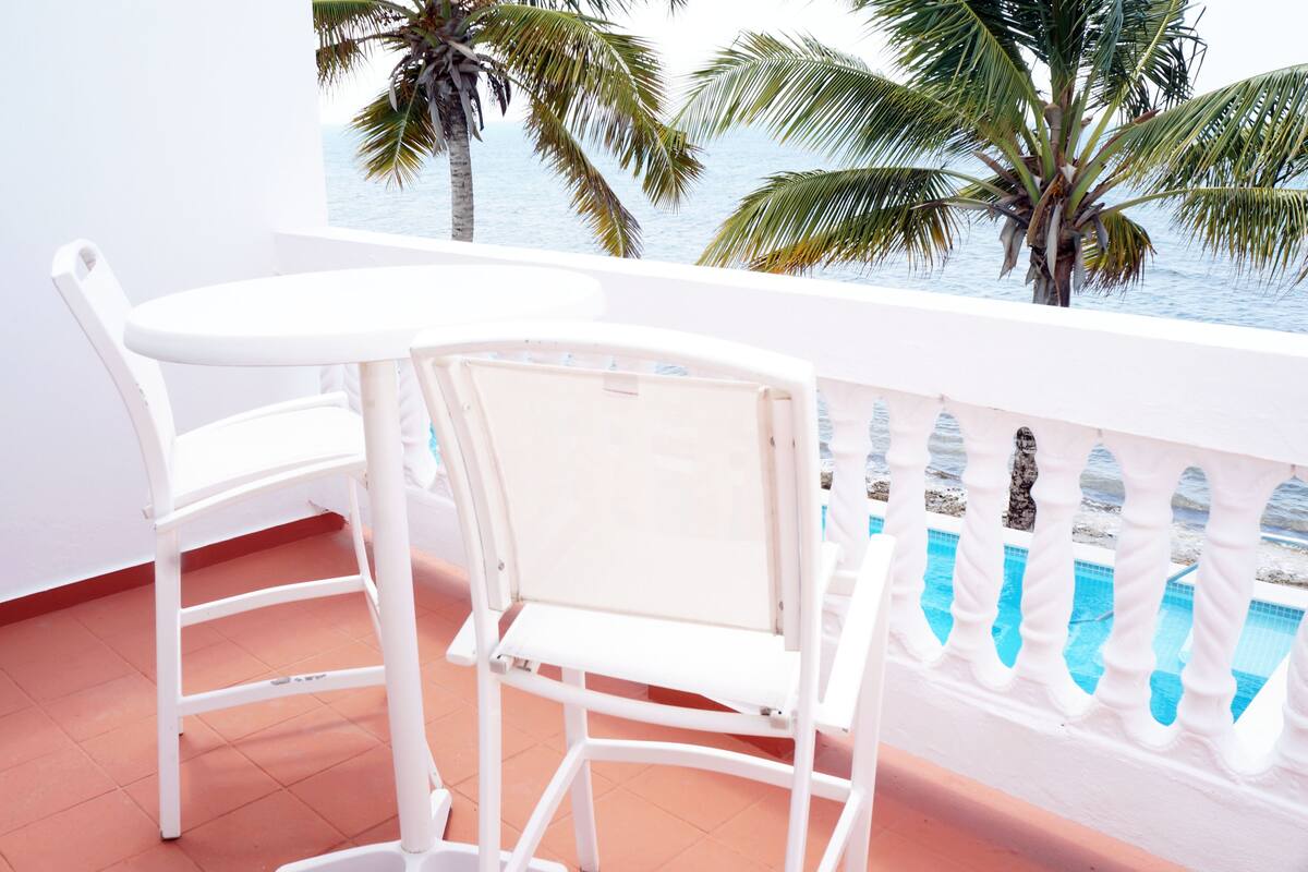 Un balcon avec des chaises blanches et une vue sur la mer et les palmiers.