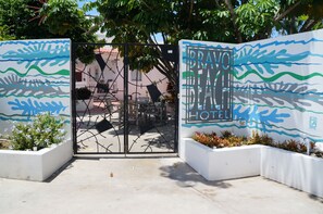 Entrada de hotel con una reja metálica, un mural con motivos de olas y un cartel que dice "BRAVO HOTEL".
