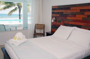 Una habitación de hotel con cama, sillón, mesita de noche y vista al océano.